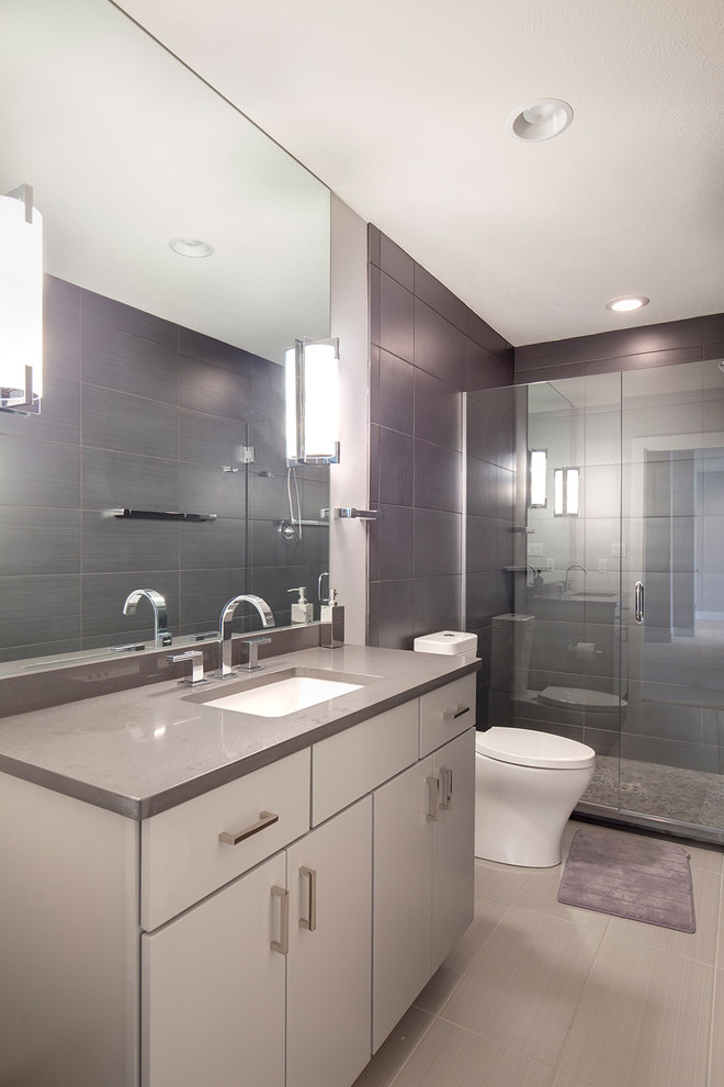 Modern inredning av ett stort badrum med dusch, med grå skåp, ett hörnbadkar, en hörndusch, en toalettstol med separat cisternkåpa, grå kakel, keramikplattor, grå väggar, klinkergolv i keramik, ett undermonterad handfat och granitbänkskiva