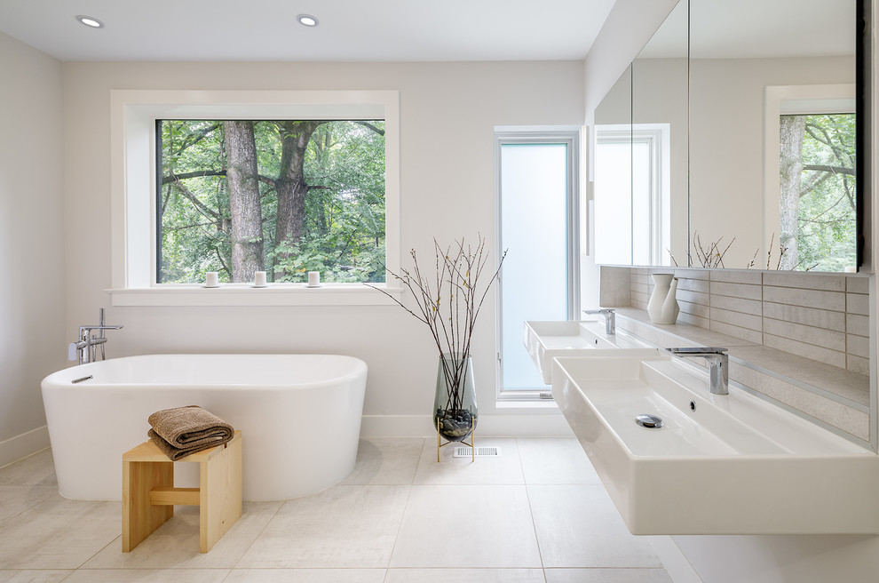 Inredning av ett 60 tals stort en-suite badrum, med ett fristående badkar, porslinskakel, klinkergolv i porslin, ett väggmonterat handfat, beiget golv, grå kakel och grå väggar