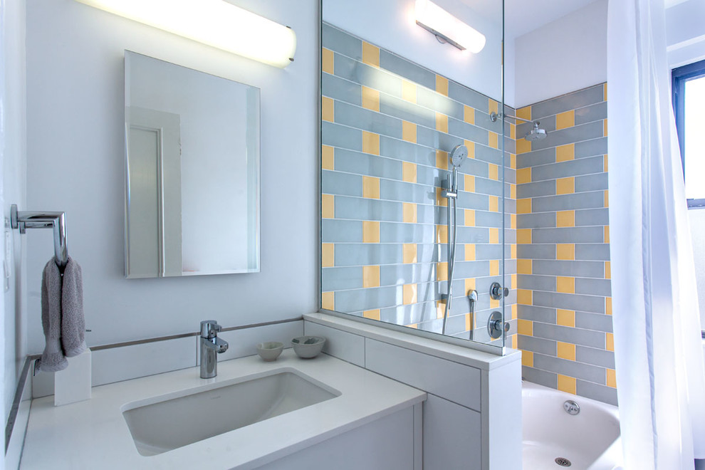 На фото: ванная комната среднего размера в стиле модернизм с плоскими фасадами, белыми фасадами, ванной в нише, душем над ванной, раздельным унитазом, серой плиткой, желтой плиткой, керамической плиткой, белыми стенами, душевой кабиной, врезной раковиной и столешницей из искусственного кварца с