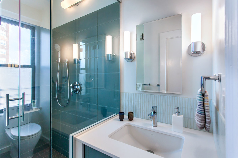 На фото: главная ванная комната среднего размера в стиле модернизм с плоскими фасадами, бирюзовыми фасадами, душем без бортиков, унитазом-моноблоком, синей плиткой, стеклянной плиткой, белыми стенами, полом из керамогранита, врезной раковиной и столешницей из искусственного кварца