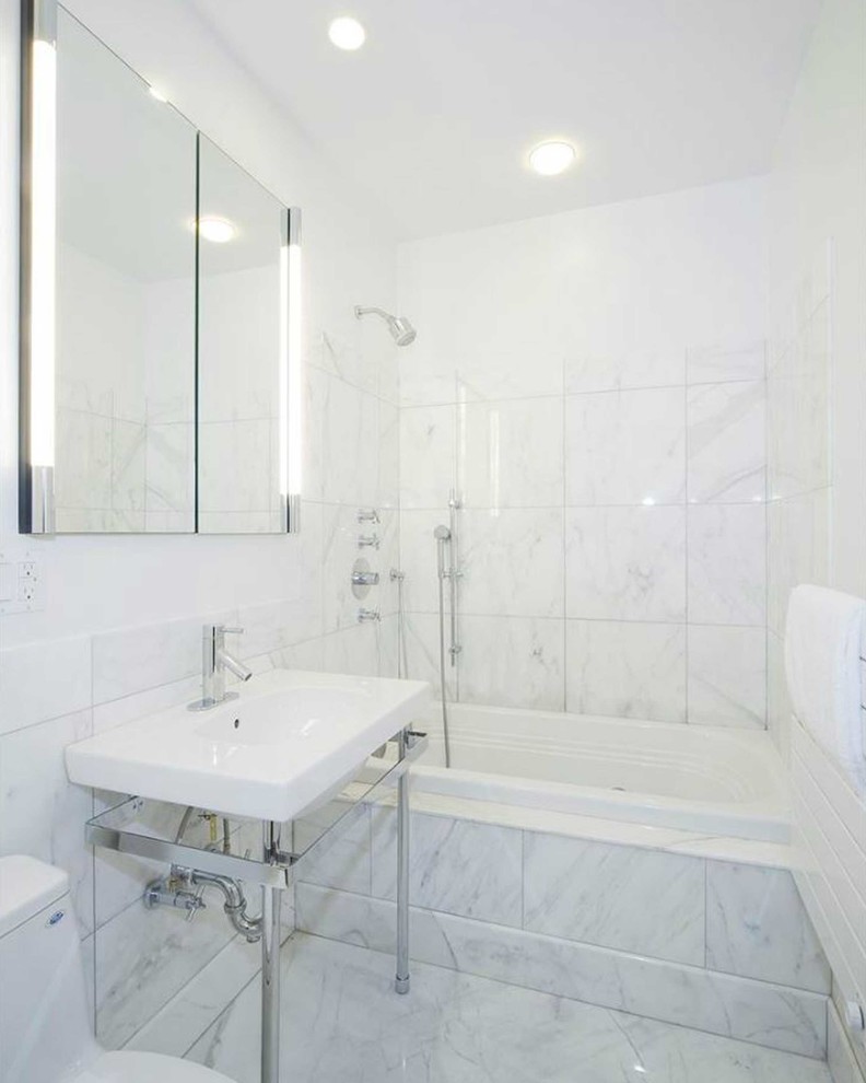 Photo of a medium sized contemporary ensuite bathroom in New York with a pedestal sink, marble worktops, a built-in bath, a shower/bath combination, a one-piece toilet, white tiles, stone tiles, white walls and marble flooring.