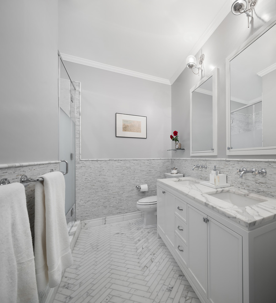 ニューヨークにあるトラディショナルスタイルのおしゃれな浴室 (アンダーカウンター洗面器、落し込みパネル扉のキャビネット、白いキャビネット、アルコーブ型シャワー、白いタイル、ボーダータイル、グレーの壁) の写真
