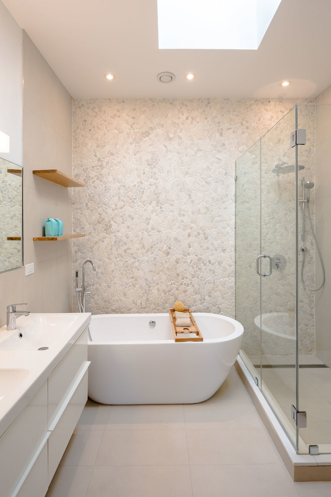 This is an example of a small modern ensuite bathroom in New York with flat-panel cabinets, white cabinets, a freestanding bath, a wall mounted toilet, beige tiles, pebble tiles, white walls, porcelain flooring, an integrated sink, solid surface worktops, beige floors, a hinged door and white worktops.