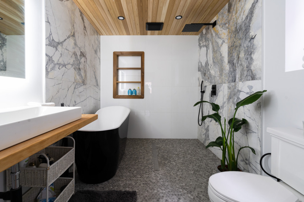 Immagine di una stanza da bagno minimal con vasca freestanding, piastrelle grigie, pavimento con piastrelle a mosaico, lavabo a bacinella, top in legno, pavimento grigio e top marrone