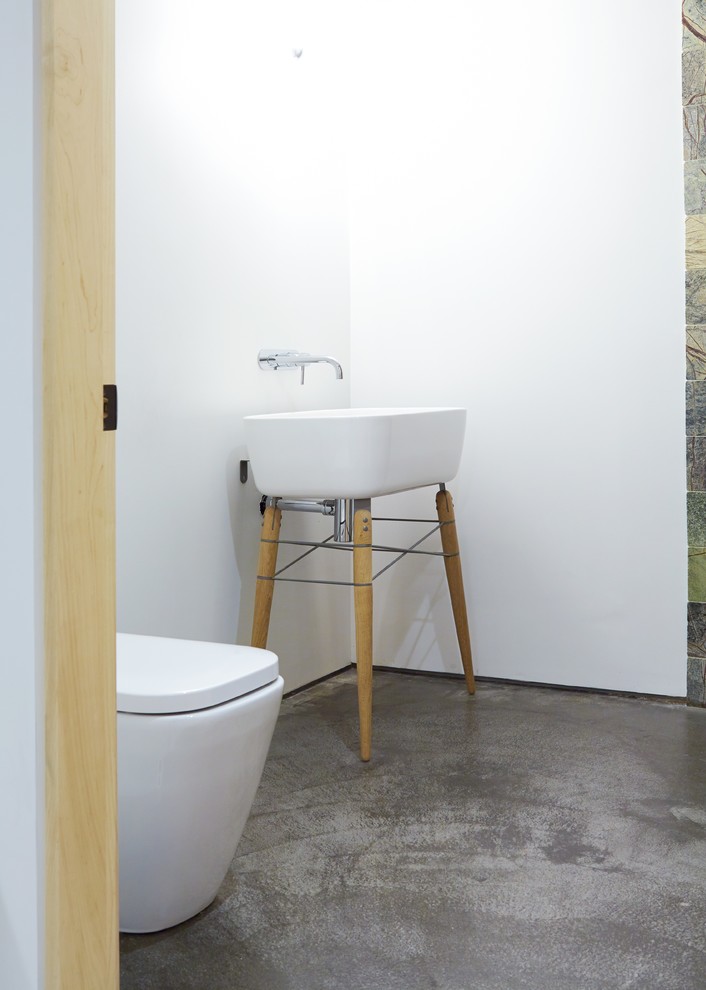 Exempel på ett mellanstort modernt badrum med dusch, med ett piedestal handfat, öppna hyllor, skåp i ljust trä, en öppen dusch, en vägghängd toalettstol, flerfärgad kakel, stenkakel, vita väggar och betonggolv