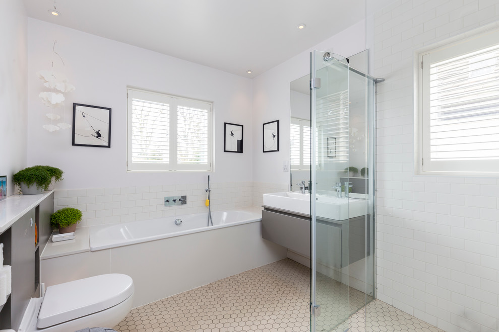 Modern inredning av ett en-suite badrum, med släta luckor, grå skåp, ett platsbyggt badkar, en vägghängd toalettstol, vit kakel, tunnelbanekakel, vita väggar och ett avlångt handfat