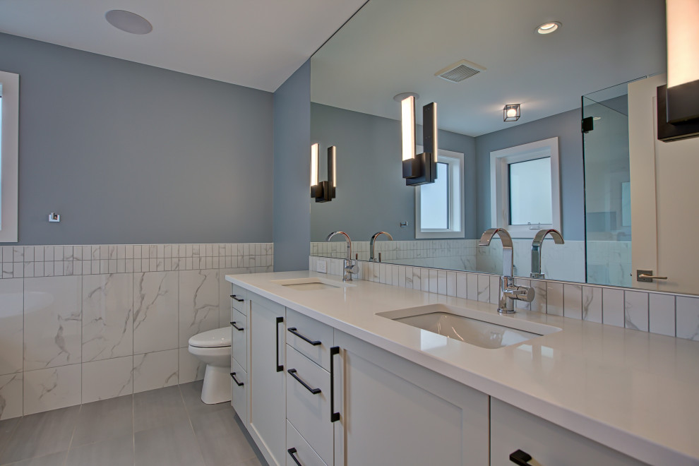 Cette image montre une salle de bain design avec un placard à porte shaker, des portes de placard blanches, un carrelage gris, un sol en carrelage de porcelaine, un lavabo encastré, un plan de toilette en quartz modifié, un sol gris, un plan de toilette blanc, meuble double vasque et meuble-lavabo encastré.