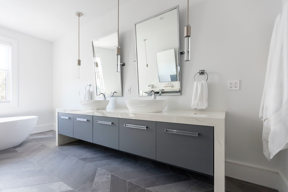 Идея дизайна: большая главная ванная комната в современном стиле с плоскими фасадами, серыми фасадами, отдельно стоящей ванной, белыми стенами, полом из сланца, настольной раковиной и мраморной столешницей