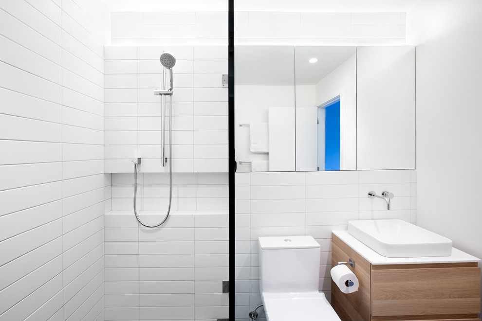 This is an example of a medium sized modern ensuite bathroom in Vancouver with a pedestal sink, flat-panel cabinets, medium wood cabinets, solid surface worktops, an alcove shower, a one-piece toilet, white tiles, ceramic tiles, white walls and porcelain flooring.