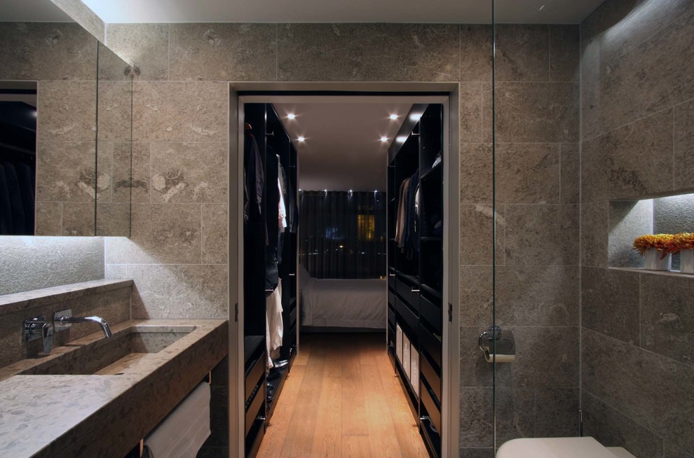Cette image montre une salle de bain principale design de taille moyenne avec un lavabo intégré, un plan de toilette en calcaire, une douche d'angle, WC à poser, un carrelage de pierre, un mur gris et un sol en calcaire.