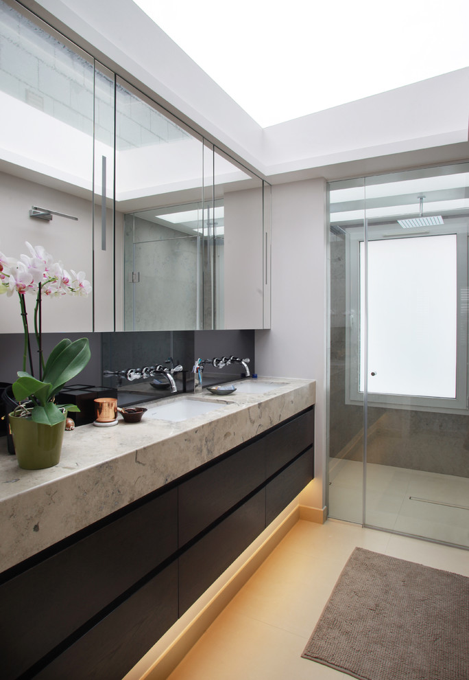 Modelo de cuarto de baño actual con lavabo bajoencimera, armarios con paneles lisos, puertas de armario negras, ducha a ras de suelo, baldosas y/o azulejos grises y ventanas