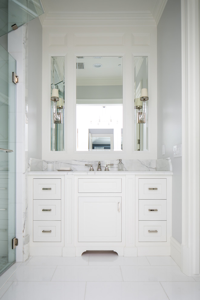 Modelo de cuarto de baño clásico renovado de tamaño medio con armarios con paneles empotrados, puertas de armario blancas, ducha empotrada, paredes grises, aseo y ducha, lavabo bajoencimera, encimera de mármol, ducha con puerta con bisagras y encimeras grises