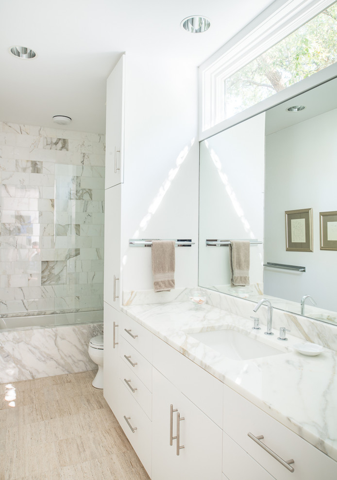 На фото: большая ванная комната в современном стиле с плоскими фасадами, белыми фасадами, полновстраиваемой ванной, душем над ванной, белыми стенами, полом из травертина, душевой кабиной, врезной раковиной и мраморной столешницей с
