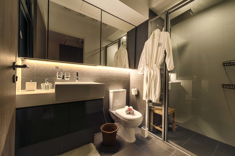 Photo of a small scandinavian ensuite bathroom in Singapore with flat-panel cabinets, black cabinets, a one-piece toilet, grey tiles, ceramic tiles, beige walls, ceramic flooring, a vessel sink and solid surface worktops.