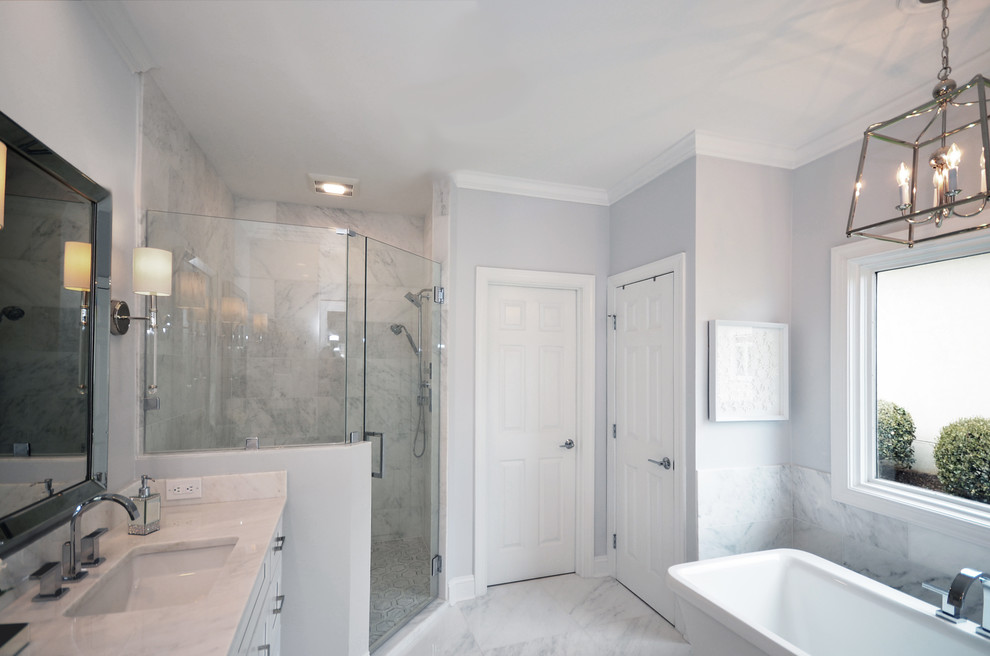 Exemple d'une salle de bain bord de mer de taille moyenne avec un placard à porte shaker, des portes de placard blanches, une baignoire indépendante, une douche d'angle, un carrelage blanc, du carrelage en marbre, un mur gris, un sol en marbre, un lavabo encastré, un plan de toilette en marbre, un sol blanc, une cabine de douche à porte battante et un plan de toilette blanc.