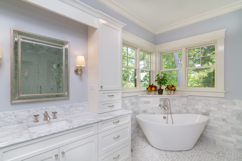 Elegant white tile and subway tile marble floor and white floor freestanding bathtub photo in Charlotte with recessed-panel cabinets, white cabinets, blue walls, an undermount sink and white countertops