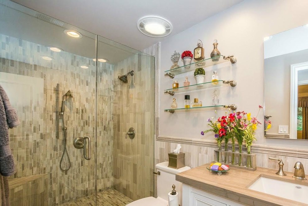 Foto på ett mellanstort vintage badrum med dusch, med luckor med infälld panel, vita skåp, en dusch i en alkov, en toalettstol med separat cisternkåpa, beige kakel, brun kakel, porslinskakel, vita väggar, träbänkskiva och dusch med gångjärnsdörr