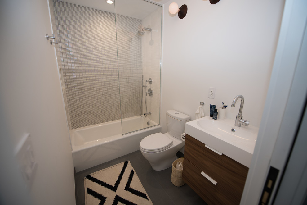 Inspiration for a medium sized contemporary ensuite bathroom in New York with flat-panel cabinets, medium wood cabinets, an alcove bath, a walk-in shower, a two-piece toilet, white tiles, cement tiles, white walls, ceramic flooring, a submerged sink, engineered stone worktops, black floors, a hinged door and white worktops.