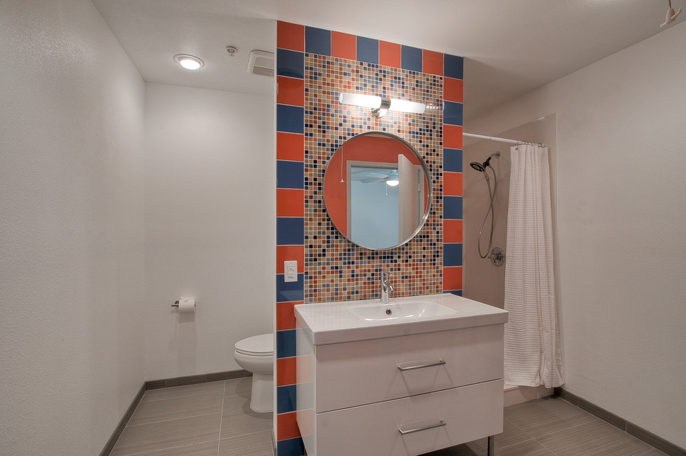 Inspiration for a small contemporary shower room bathroom in Dallas with multi-coloured tiles, mosaic tiles, flat-panel cabinets, white cabinets, an alcove shower, a one-piece toilet, white walls, porcelain flooring, an integrated sink and solid surface worktops.