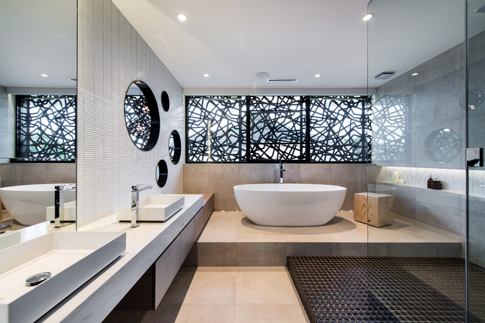 Inredning av ett modernt en-suite badrum, med släta luckor, skåp i mörkt trä, ett fristående badkar, en öppen dusch, grå kakel, ett fristående handfat och med dusch som är öppen