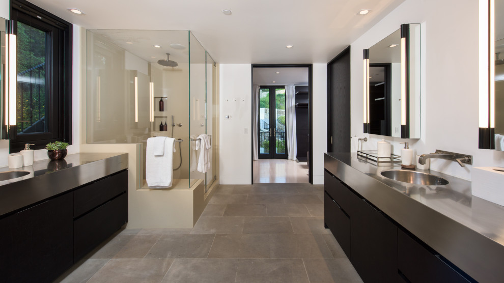 Inspiration for a large contemporary ensuite bathroom in Los Angeles with flat-panel cabinets, black cabinets, a freestanding bath, a corner shower, a built-in sink, stainless steel worktops, a hinged door, double sinks and a built in vanity unit.