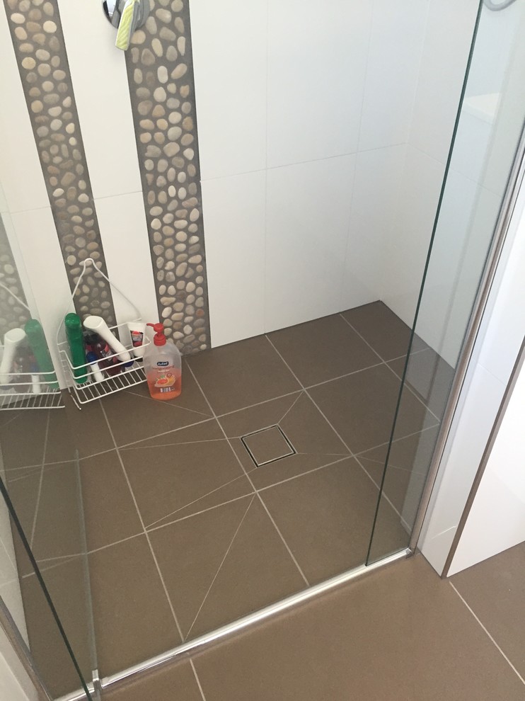 Exempel på ett litet modernt badrum med dusch, med släta luckor, vita skåp, en dusch i en alkov, porslinskakel, vita väggar, cementgolv, ett integrerad handfat, brunt golv och dusch med gångjärnsdörr