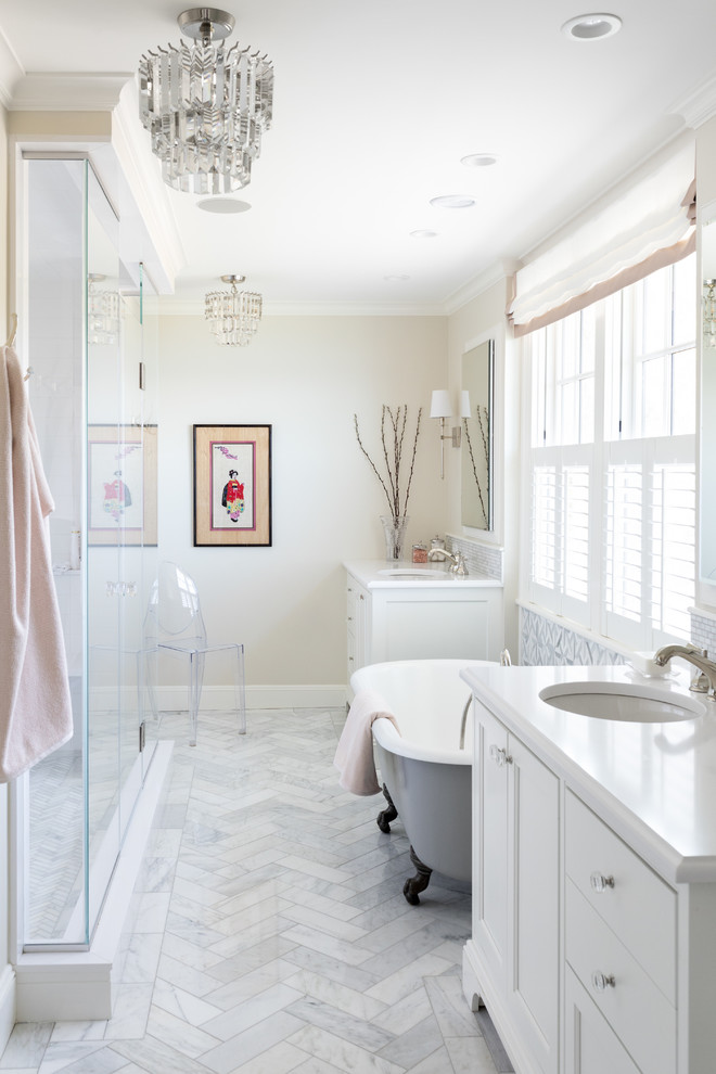 Diseño de cuarto de baño principal marinero con puertas de armario blancas, encimeras blancas, bañera con patas, paredes beige, suelo de mármol, lavabo bajoencimera y armarios con paneles empotrados