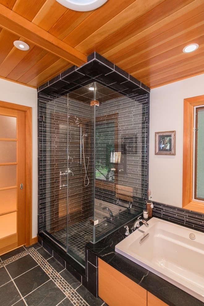 This is an example of a large contemporary ensuite bathroom in New York with a submerged sink, flat-panel cabinets, light wood cabinets, granite worktops, a built-in bath, a corner shower, a one-piece toilet, black tiles, ceramic tiles, white walls and ceramic flooring.