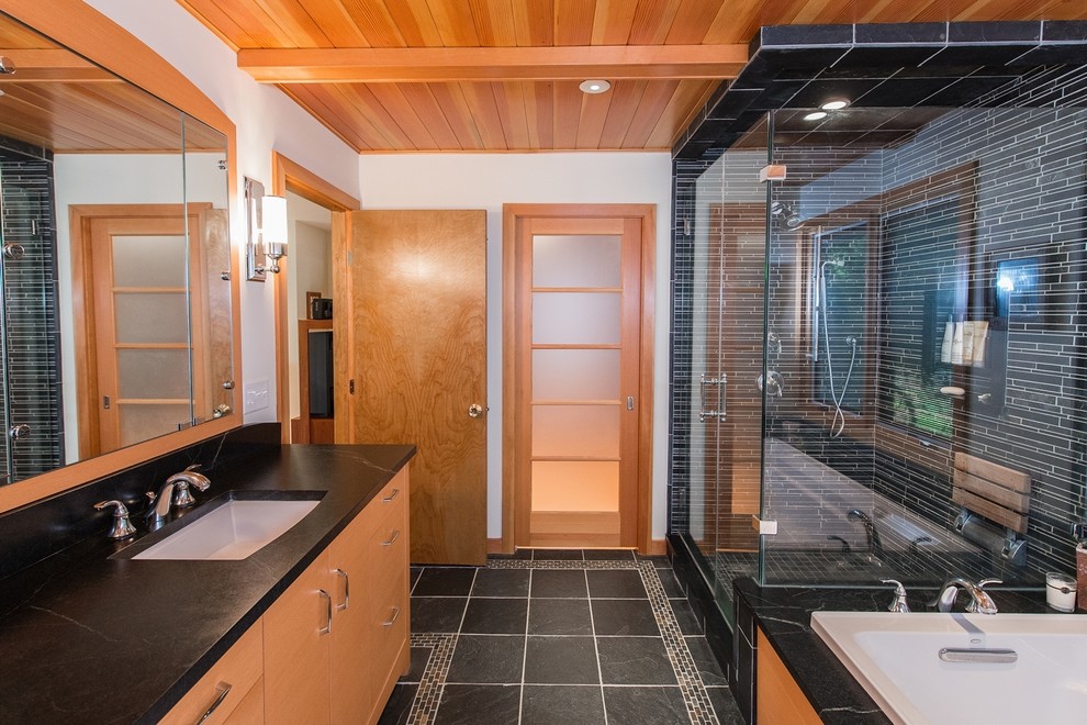 На фото: ванная комната в современном стиле с врезной раковиной, плоскими фасадами, фасадами цвета дерева среднего тона, столешницей из гранита, накладной ванной, душем в нише, унитазом-моноблоком, черной плиткой и удлиненной плиткой с