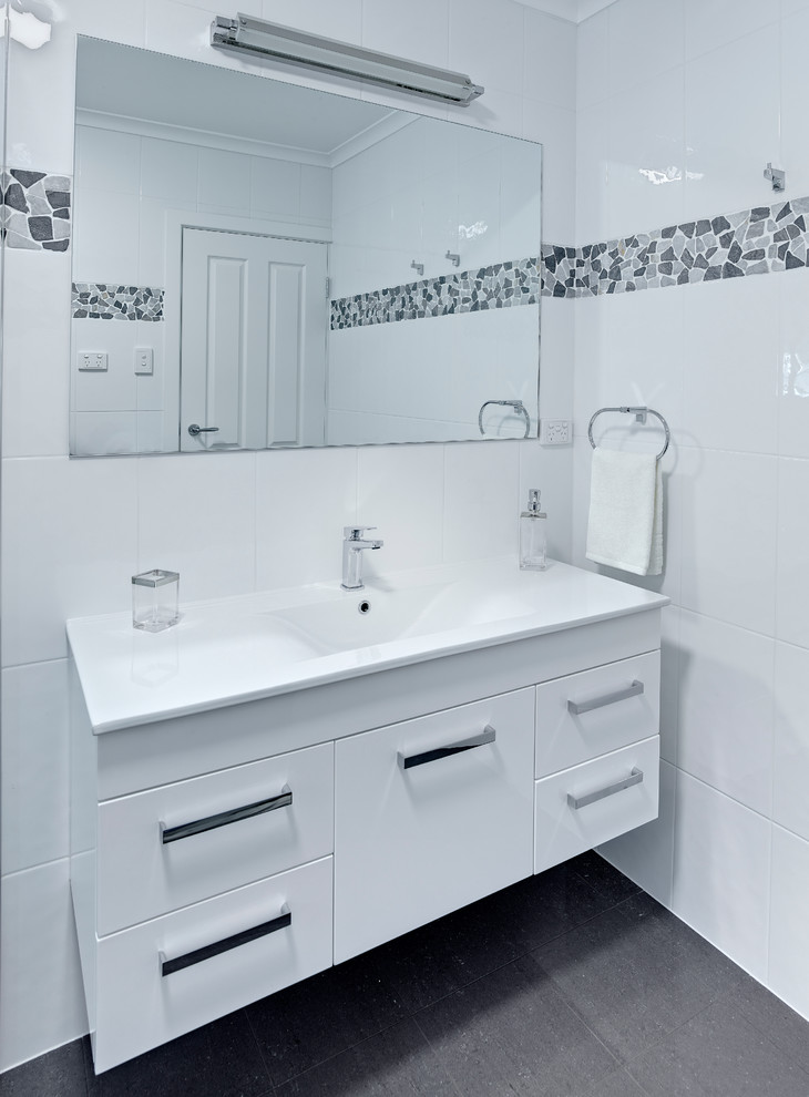 Стильный дизайн: маленькая главная ванная комната в стиле модернизм с монолитной раковиной, белыми фасадами, душем над ванной, белой плиткой, белыми стенами и полом из керамогранита для на участке и в саду - последний тренд