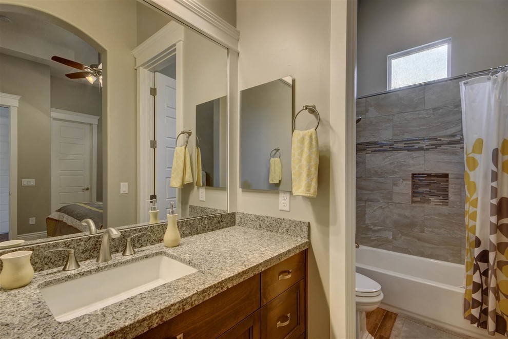 Inredning av ett klassiskt mellanstort badrum med dusch, med ett hörnbadkar, en dusch/badkar-kombination, en toalettstol med separat cisternkåpa, grå kakel, porslinskakel, grå väggar, mellanmörkt trägolv, skåp i mörkt trä, ett undermonterad handfat och granitbänkskiva
