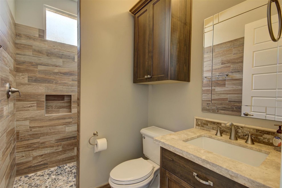 Inspiration for a mid-sized transitional 3/4 beige tile and pebble tile medium tone wood floor walk-in shower remodel in Phoenix with recessed-panel cabinets, dark wood cabinets, a two-piece toilet, gray walls, an undermount sink and granite countertops
