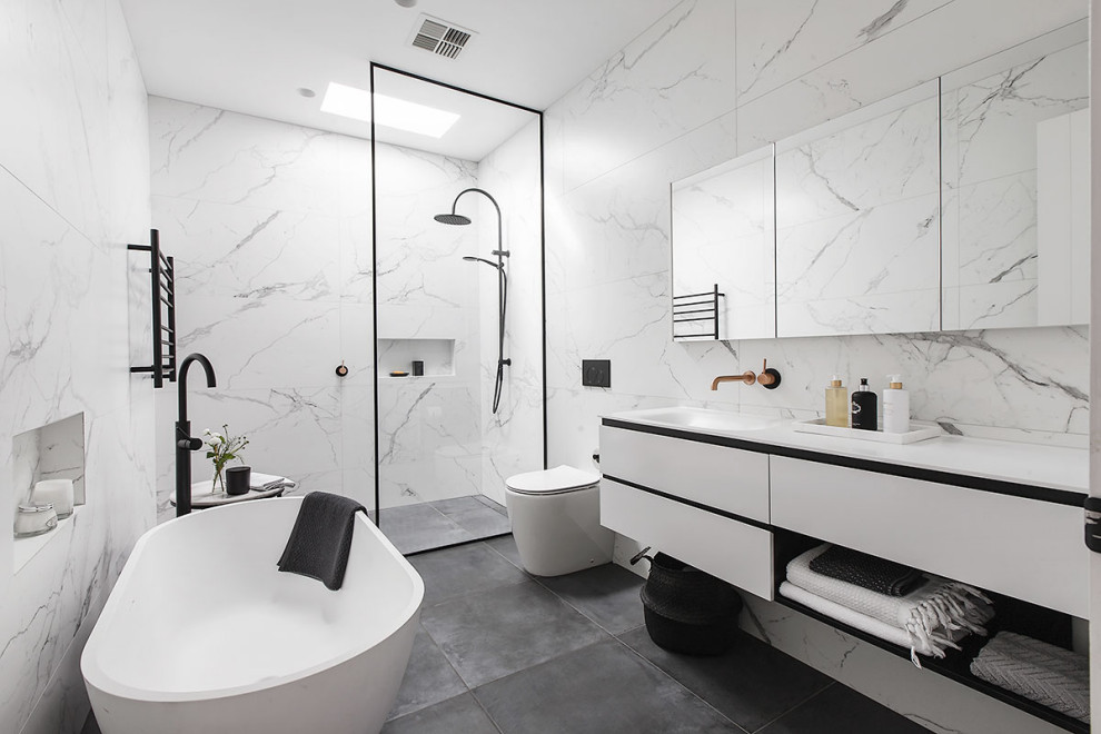 This is an example of a contemporary bathroom in Melbourne with flat-panel cabinets, white cabinets, a freestanding bath, a built-in shower, white tiles, an integrated sink, grey floors, an open shower, white worktops and a floating vanity unit.