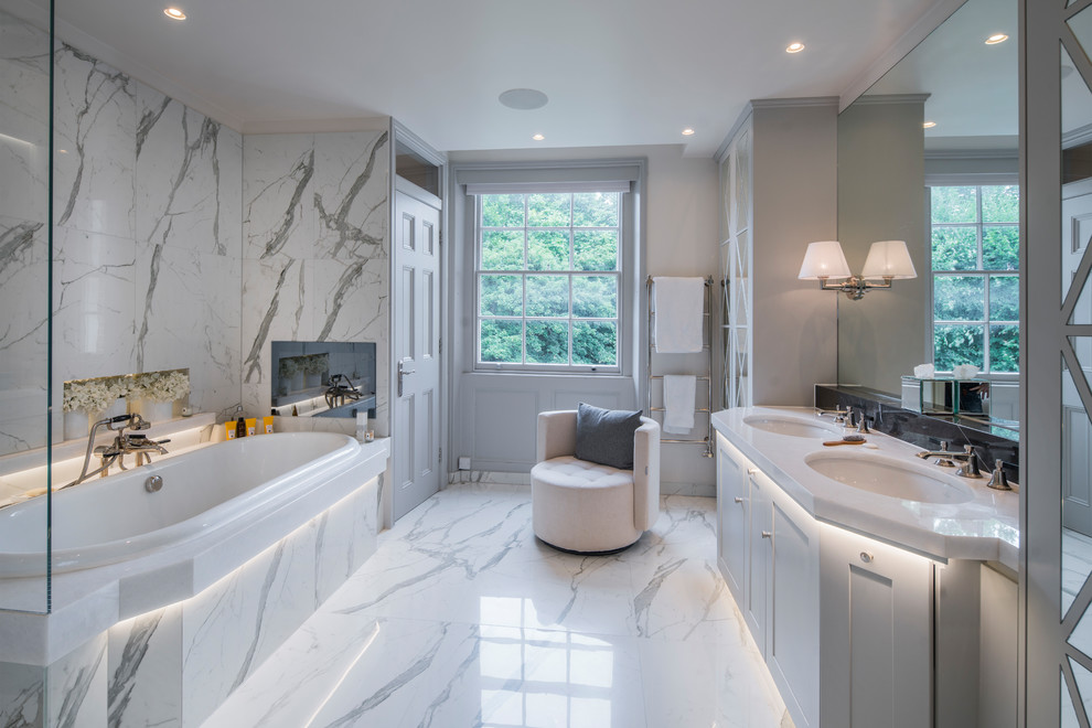 Cette image montre une salle de bain traditionnelle de taille moyenne avec un placard avec porte à panneau encastré, des portes de placard blanches, une baignoire posée, du carrelage en marbre, un mur blanc, un sol en marbre et un sol blanc.