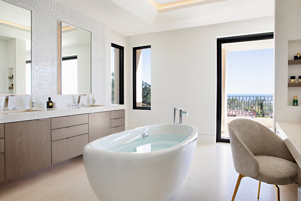 Inspiration for a contemporary ensuite bathroom in Orange County with flat-panel cabinets, medium wood cabinets, a freestanding bath, grey tiles, white walls, an integrated sink, beige floors and white worktops.