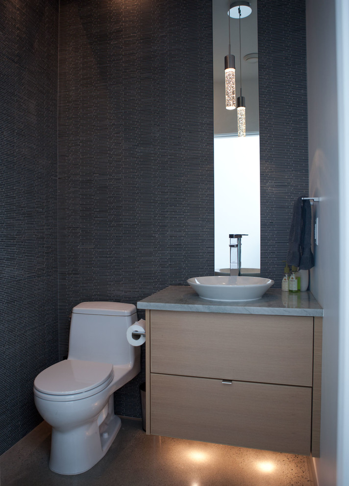Cette photo montre une petite salle de bain tendance en bois clair avec un lavabo posé, un placard à porte plane, un plan de toilette en granite, WC à poser, un carrelage gris, un carrelage en pâte de verre, un mur gris et sol en béton ciré.