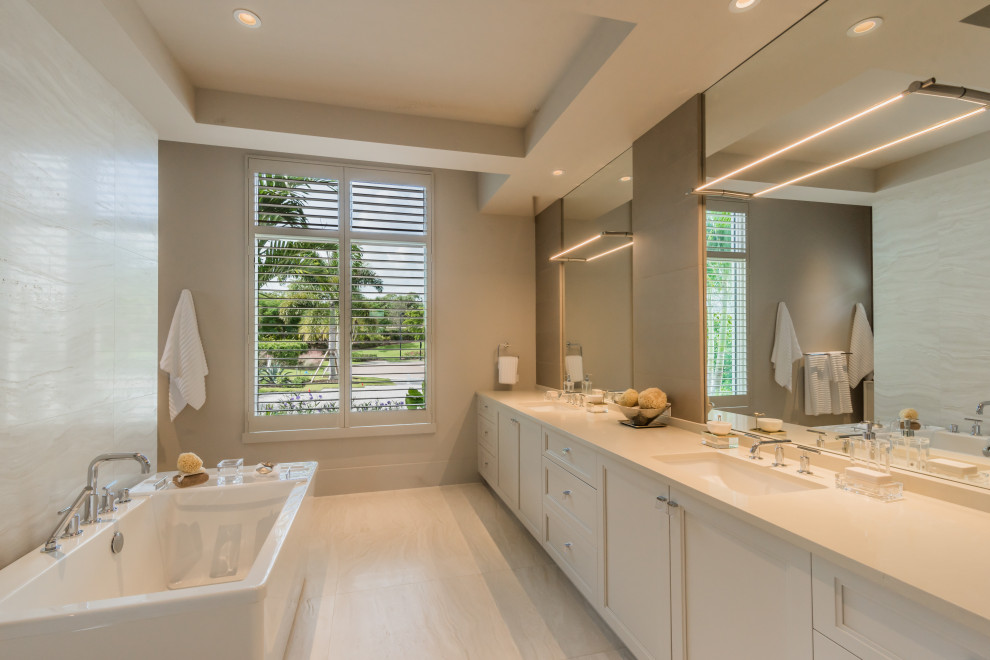 Freestanding bathtub - large mediterranean master beige tile and porcelain tile porcelain tile and beige floor freestanding bathtub idea in Miami with recessed-panel cabinets, white cabinets, gray walls, an undermount sink and beige countertops