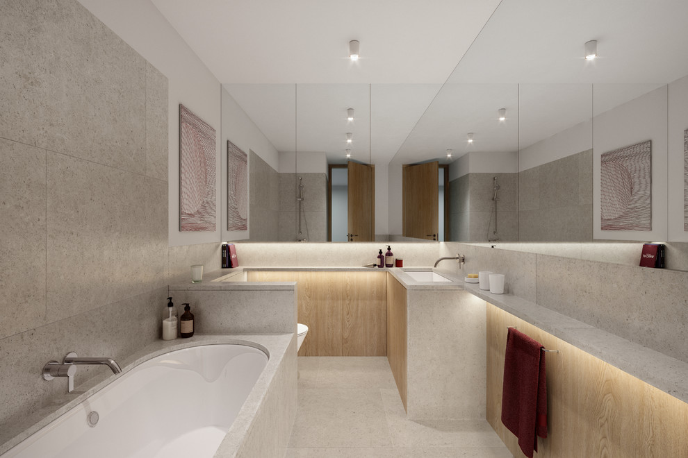 Cette image montre une salle de bain principale design en bois clair avec un placard à porte plane, une baignoire posée, un carrelage gris, un mur blanc, un lavabo encastré, un sol gris et un plan de toilette gris.