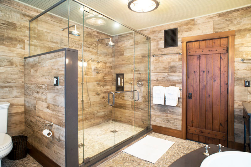 Inspiration for a large rustic ensuite bathroom in New York with medium wood cabinets, a built-in bath, a double shower, a two-piece toilet, grey tiles, ceramic tiles, grey walls, pebble tile flooring, a submerged sink, granite worktops, grey floors, a hinged door and grey worktops.