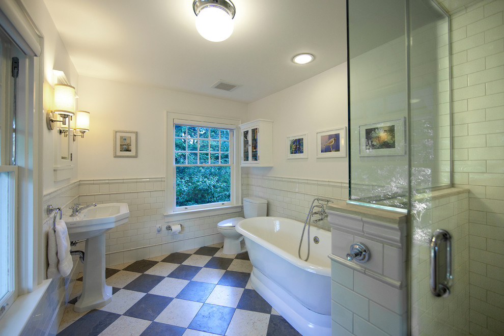 This is an example of a medium sized traditional ensuite bathroom in New York with a freestanding bath, an alcove shower, a two-piece toilet, white tiles, metro tiles, white walls, lino flooring and a pedestal sink.