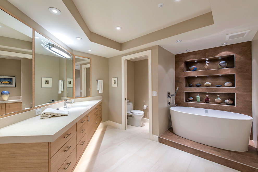 This is an example of a contemporary ensuite bathroom in Miami with flat-panel cabinets, light wood cabinets, a freestanding bath, beige walls and porcelain flooring.