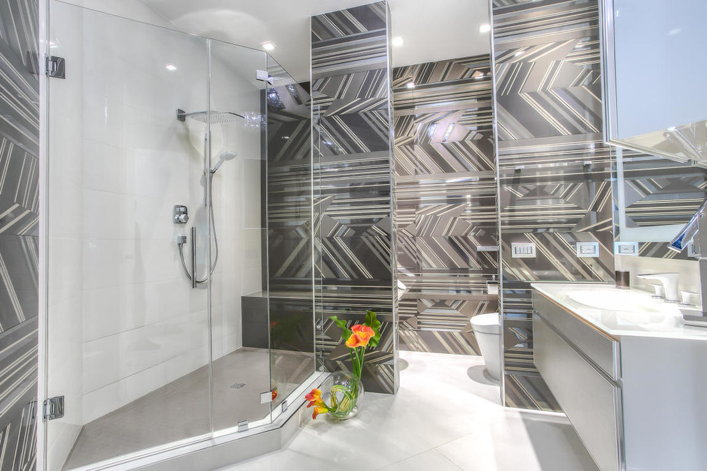 На фото: огромная главная ванная комната в современном стиле с плоскими фасадами, серыми фасадами, накладной ванной, угловым душем, раздельным унитазом, разноцветной плиткой, керамогранитной плиткой, белыми стенами, полом из керамогранита, врезной раковиной и стеклянной столешницей