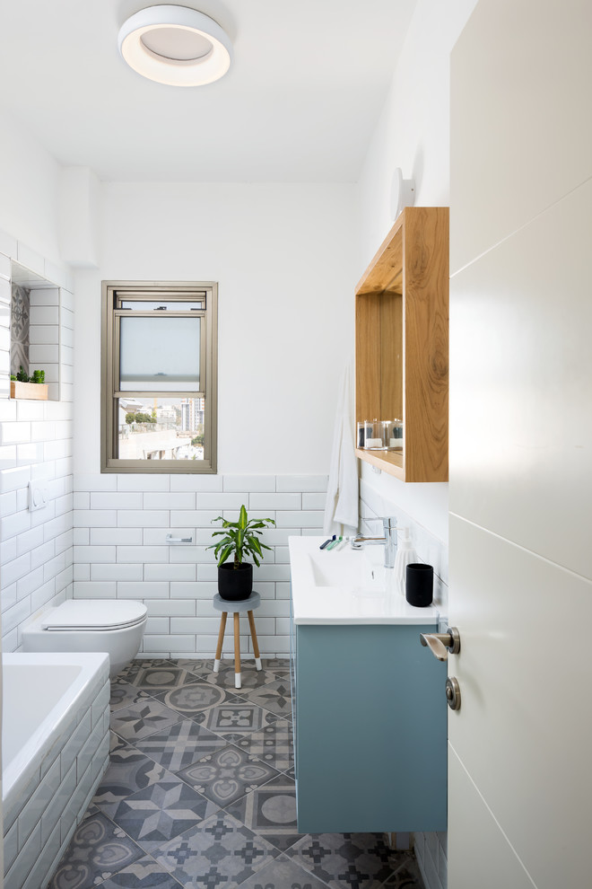 Idée de décoration pour une salle d'eau design avec des portes de placard bleues, une baignoire d'angle, WC suspendus, un carrelage blanc, un carrelage métro, un mur blanc, un lavabo intégré, un sol gris et un plan de toilette blanc.
