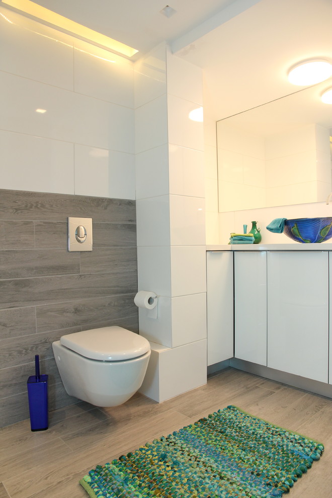 Cette image montre une salle de bain design avec un placard à porte vitrée, des portes de placard blanches, une douche d'angle, WC suspendus, un carrelage gris, des carreaux de céramique, un mur blanc, un sol en carrelage de céramique et un plan de toilette en quartz.