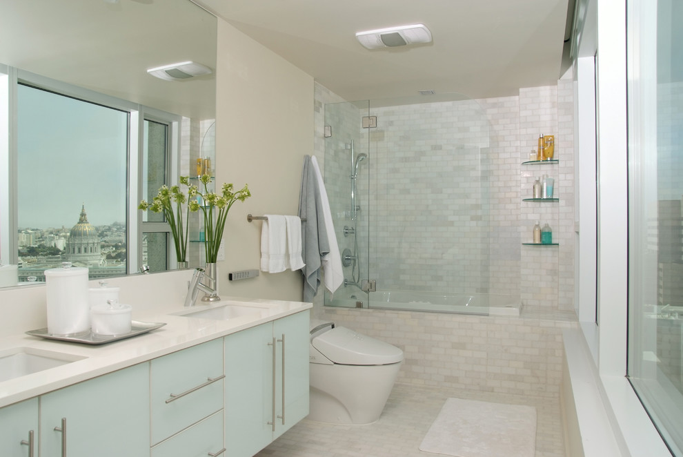 This is an example of a contemporary bathroom in San Francisco with a submerged sink, flat-panel cabinets, blue cabinets, a built-in bath, a shower/bath combination, white tiles and beige walls.