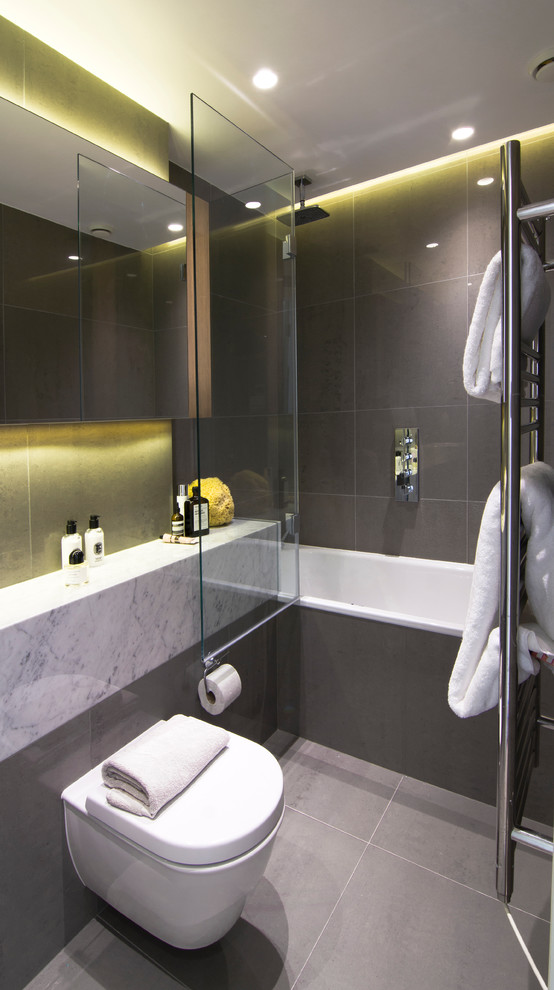 Inspiration för mellanstora moderna badrum, med marmorbänkskiva, en dusch/badkar-kombination, en vägghängd toalettstol, porslinskakel, klinkergolv i porslin, ett badkar i en alkov och grå kakel