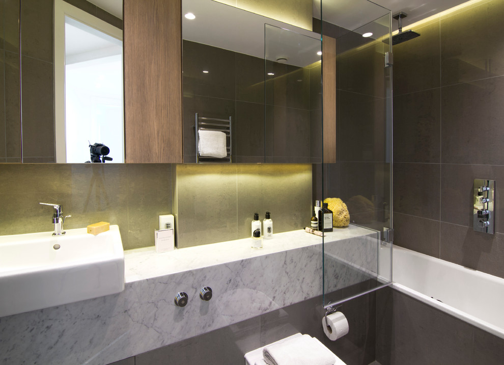 Medium sized contemporary family bathroom in London with marble worktops, a built-in bath, a shower/bath combination, a wall mounted toilet, brown tiles, porcelain tiles and porcelain flooring.