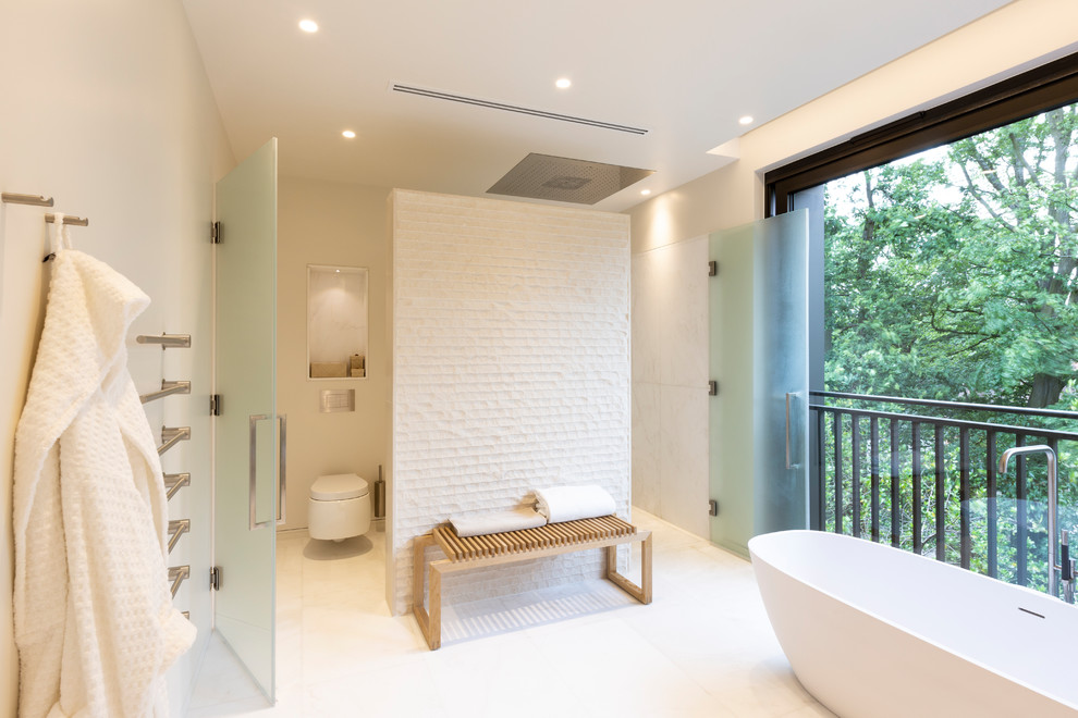 Imagen de cuarto de baño principal contemporáneo grande con bañera exenta, sanitario de pared, baldosas y/o azulejos blancos, paredes beige, suelo beige y encimeras beige