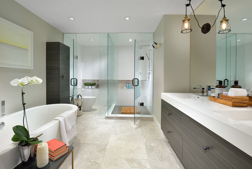 Design ideas for a medium sized modern ensuite bathroom in Toronto with an integrated sink, flat-panel cabinets, grey cabinets, solid surface worktops, a freestanding bath, a corner shower, a two-piece toilet, grey tiles, stone tiles, grey walls and marble flooring.