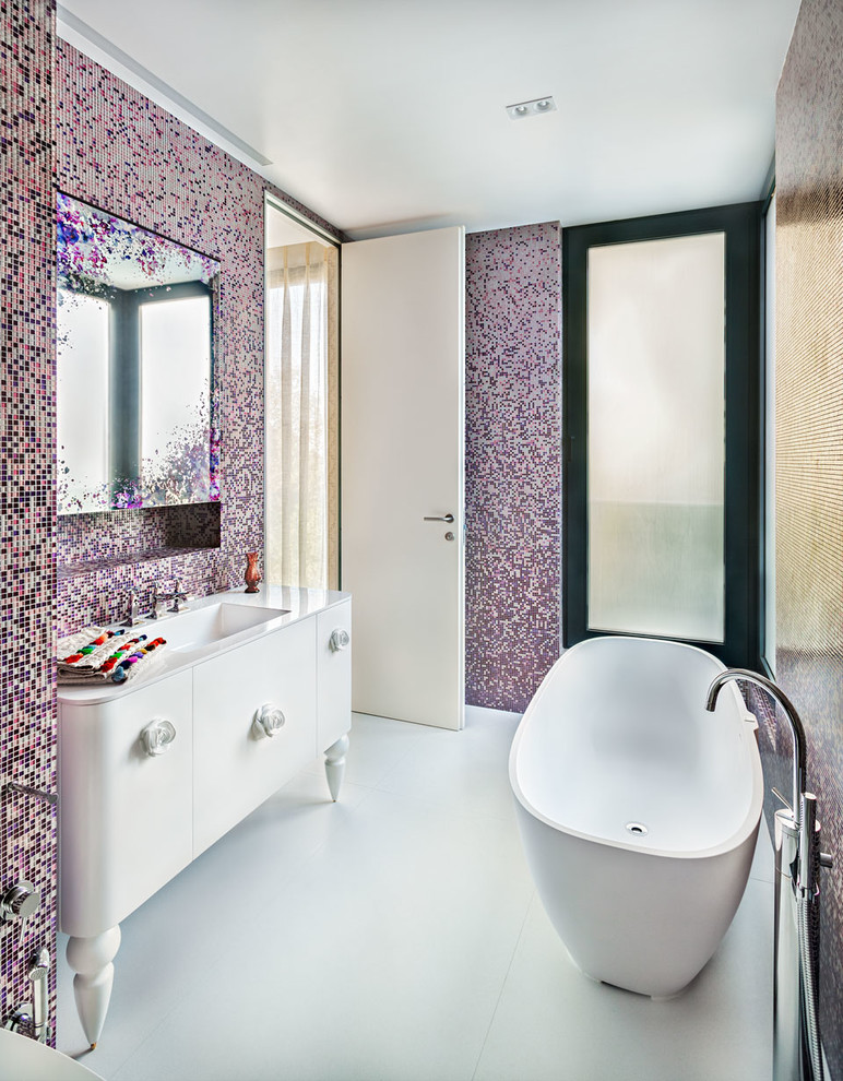 Пример оригинального дизайна: ванная комната в современном стиле с белыми фасадами, отдельно стоящей ванной, разноцветной плиткой, розовой плиткой, монолитной раковиной и плоскими фасадами